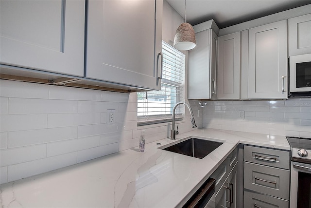 kitchen featuring tasteful backsplash, white microwave, stainless steel electric range oven, gray cabinets, and a sink