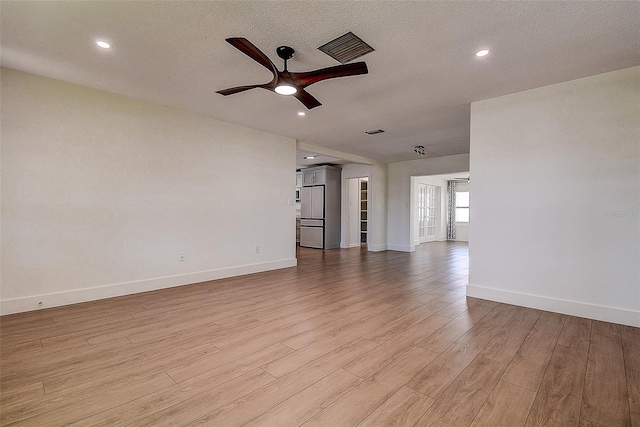 unfurnished living room with baseboards, light wood-style flooring, visible vents, and a textured ceiling