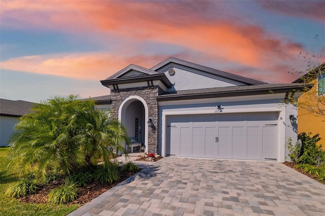 view of front facade with stone siding, decorative driveway, an attached garage, and stucco siding