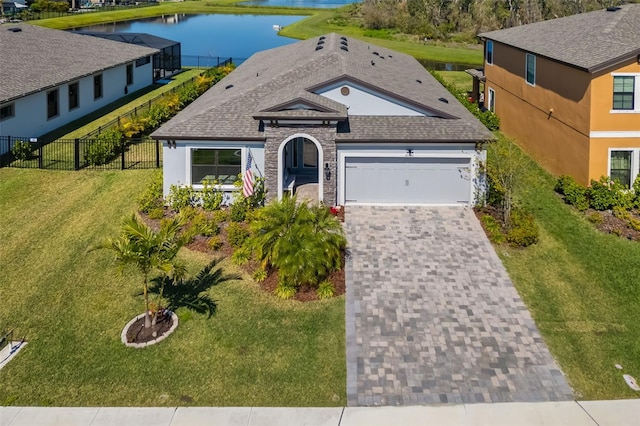 view of front of home with a water view, an attached garage, fence, decorative driveway, and a front yard