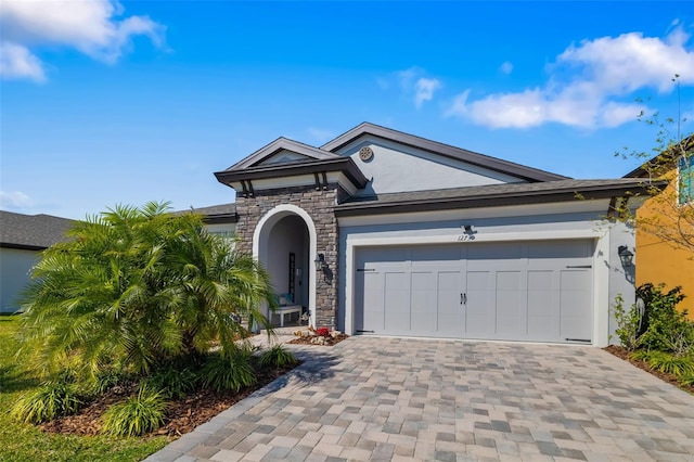 view of front of property with stone siding, decorative driveway, an attached garage, and stucco siding