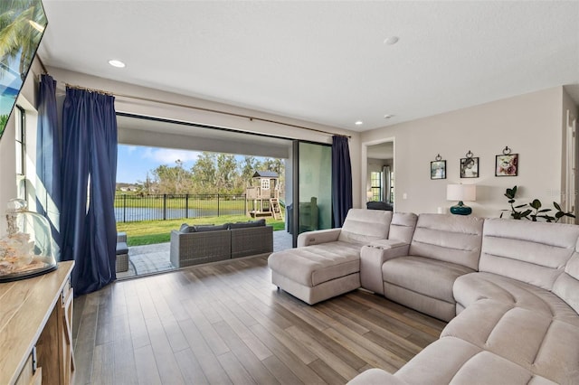 living room featuring recessed lighting, a water view, a textured ceiling, and wood finished floors