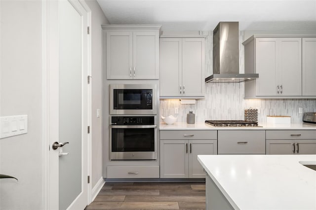 kitchen with appliances with stainless steel finishes, dark wood-style flooring, gray cabinets, and wall chimney exhaust hood