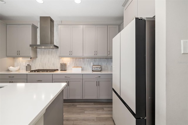 kitchen featuring wall chimney range hood, gray cabinetry, stainless steel gas cooktop, and freestanding refrigerator