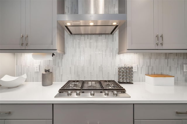 kitchen featuring wall chimney exhaust hood, gray cabinets, light countertops, and stainless steel gas stovetop