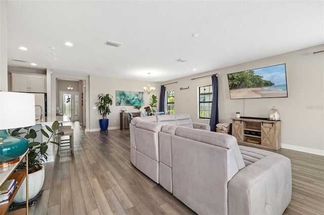 living area with light wood finished floors, recessed lighting, visible vents, an inviting chandelier, and baseboards