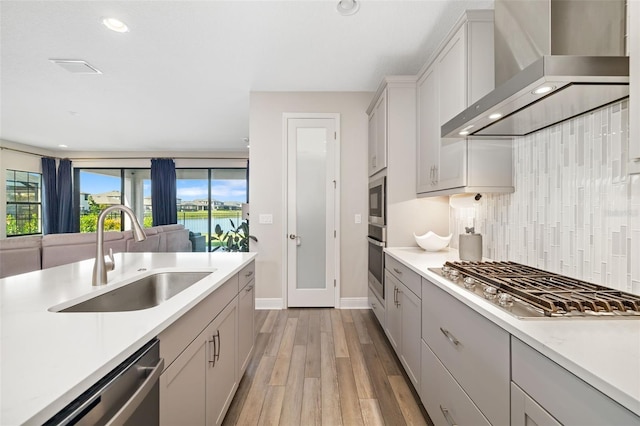 kitchen with stainless steel appliances, a sink, light countertops, backsplash, and wall chimney exhaust hood