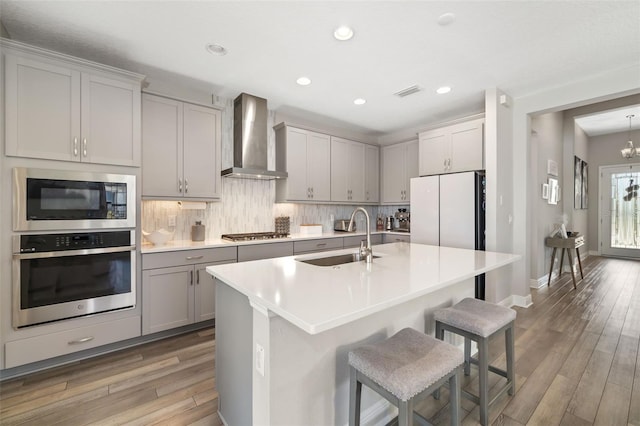 kitchen with light wood-style floors, gray cabinets, stainless steel appliances, wall chimney range hood, and a sink