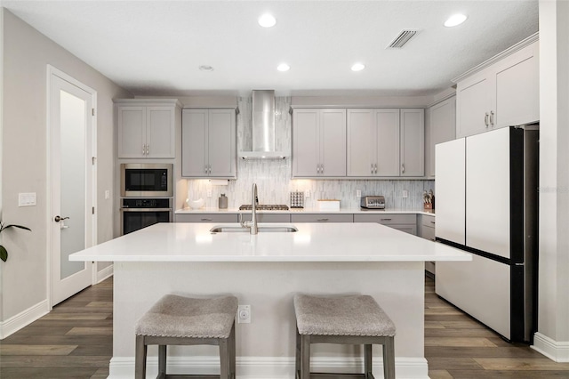 kitchen featuring dark wood finished floors, wall chimney exhaust hood, a sink, stainless steel appliances, and backsplash