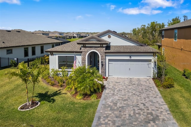 view of front of house with an attached garage, fence, stone siding, decorative driveway, and a front yard