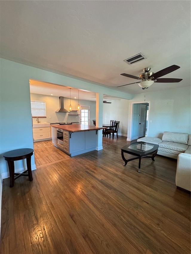 kitchen with wood finished floors, wood counters, visible vents, open floor plan, and wall chimney range hood