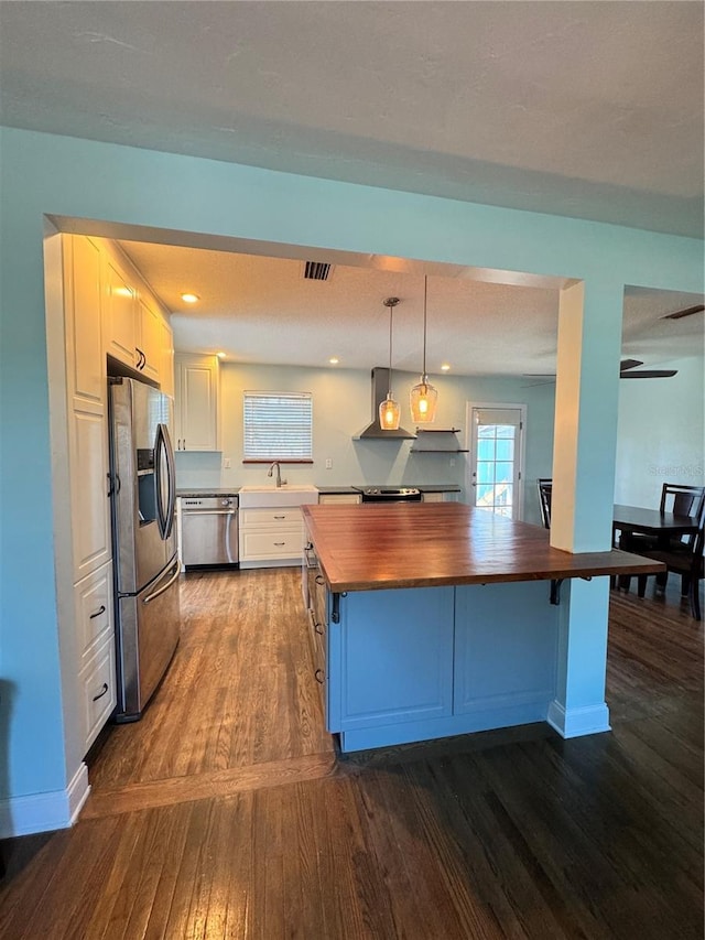 kitchen featuring butcher block countertops, white cabinets, appliances with stainless steel finishes, dark wood-style floors, and wall chimney exhaust hood