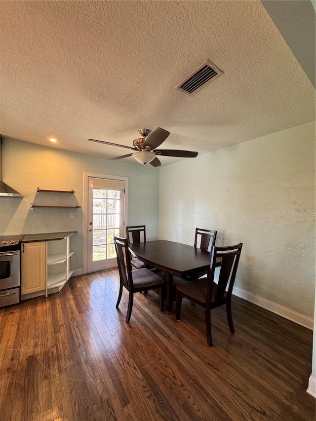 dining area featuring ceiling fan, a textured wall, dark wood-type flooring, visible vents, and baseboards