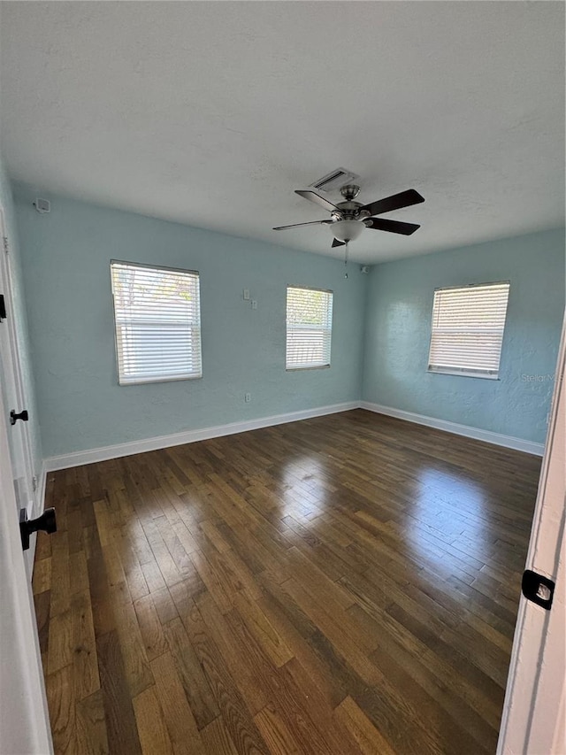 empty room featuring dark wood-type flooring, a ceiling fan, and baseboards