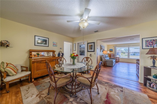 dining room featuring a ceiling fan, a textured ceiling, visible vents, and wood finished floors