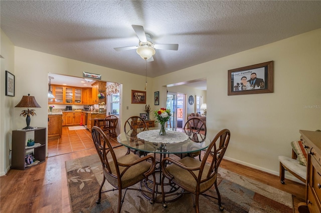 dining space featuring ceiling fan, light wood finished floors, a textured ceiling, and baseboards