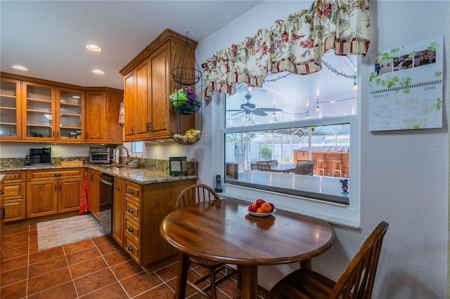 kitchen featuring stone counters, dark tile patterned flooring, brown cabinets, and glass insert cabinets