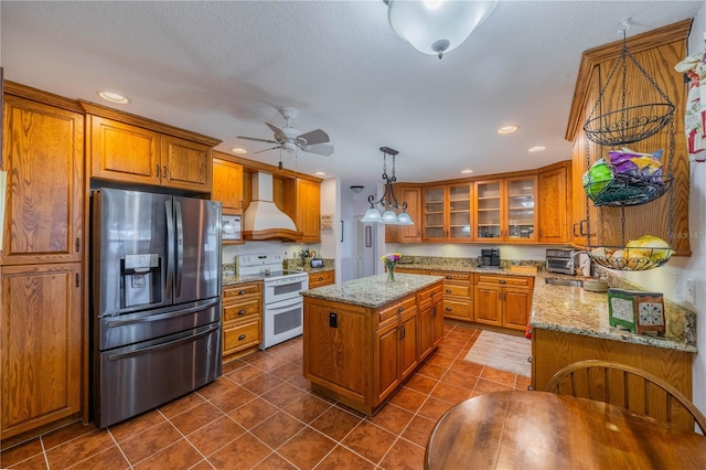 kitchen featuring range with two ovens, custom exhaust hood, stainless steel fridge, and brown cabinets