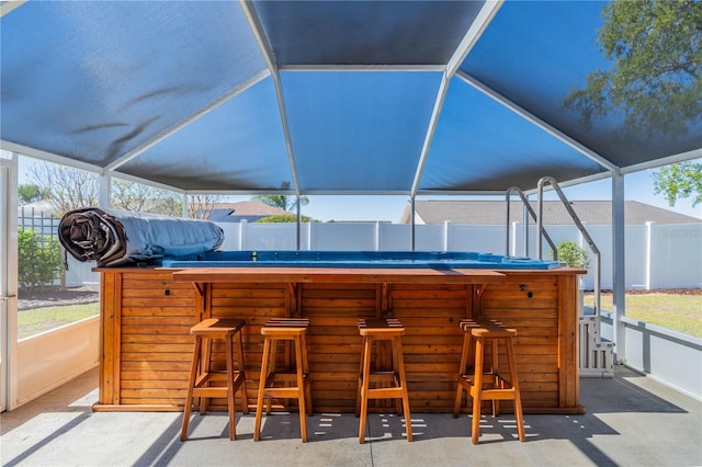 view of patio / terrace featuring outdoor dry bar, glass enclosure, and fence