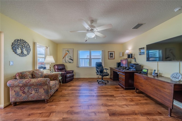 home office featuring ceiling fan, a textured ceiling, wood finished floors, visible vents, and baseboards