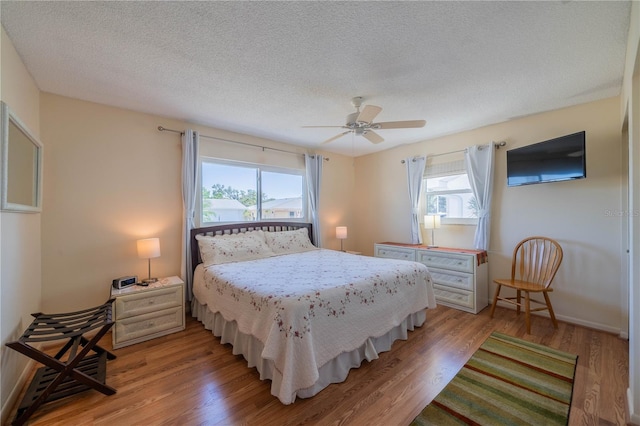 bedroom with a textured ceiling, baseboards, light wood-style flooring, and a ceiling fan