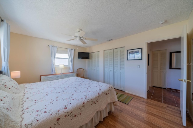 bedroom featuring a textured ceiling, ceiling fan, wood finished floors, baseboards, and two closets