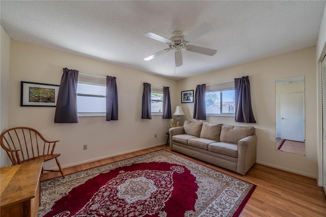 living area with light wood-style floors, baseboards, a ceiling fan, and a textured ceiling