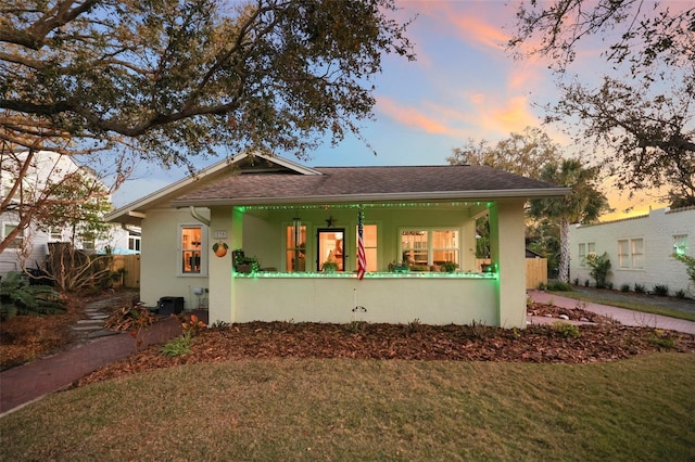 bungalow-style home featuring a shingled roof, covered porch, a front lawn, and stucco siding