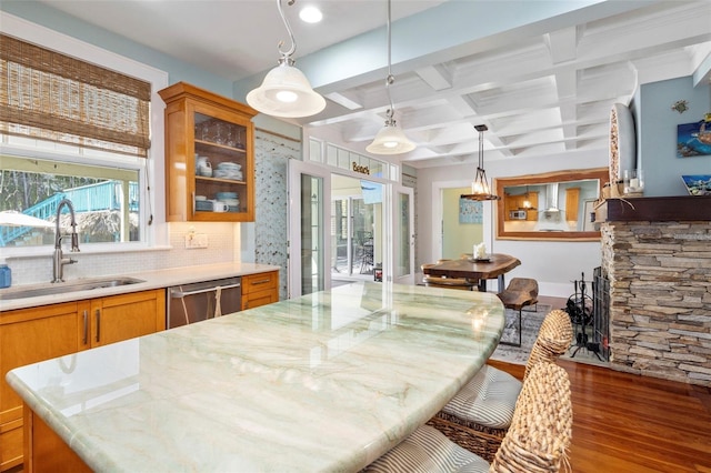 kitchen featuring coffered ceiling, dishwasher, brown cabinets, wood finished floors, and a sink