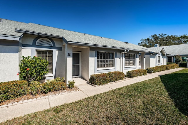 view of front of house with stucco siding, a shingled roof, and a front lawn