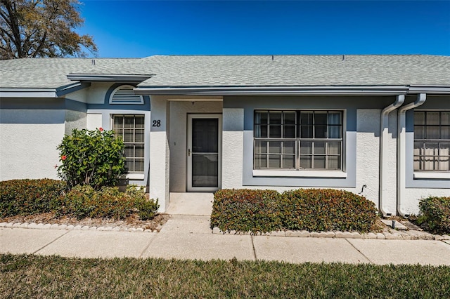 doorway to property featuring stucco siding and a shingled roof