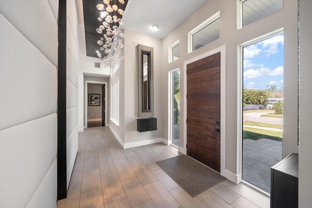 foyer entrance with a wealth of natural light, visible vents, an inviting chandelier, and baseboards