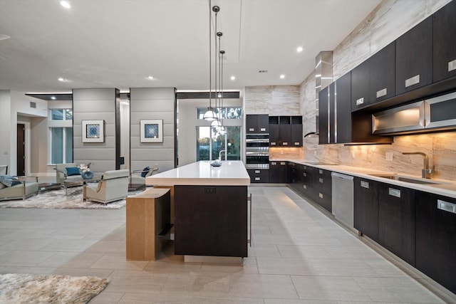 kitchen with an island with sink, a sink, decorative backsplash, light countertops, and appliances with stainless steel finishes