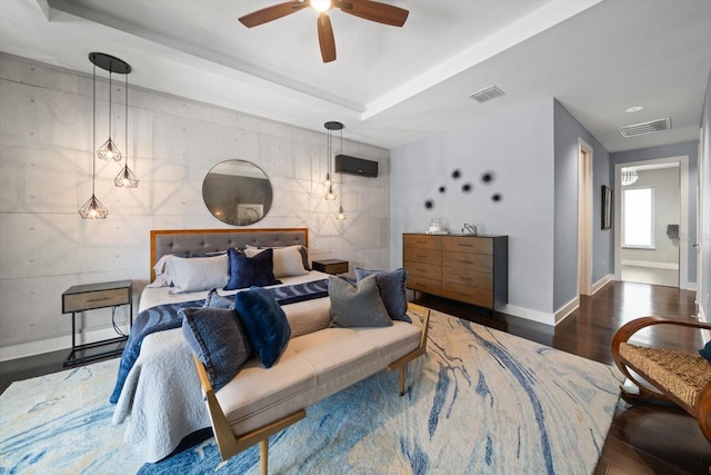 bedroom with visible vents, baseboards, a tray ceiling, and wood finished floors