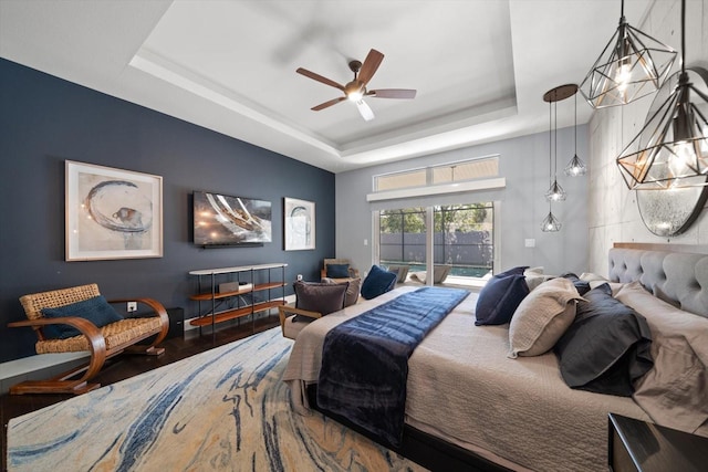 bedroom with access to exterior, a tray ceiling, ceiling fan with notable chandelier, and wood finished floors