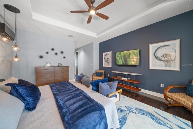 bedroom with visible vents, a tray ceiling, wood finished floors, baseboards, and ceiling fan