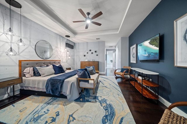 bedroom featuring wood finished floors, baseboards, a tray ceiling, ceiling fan, and an accent wall