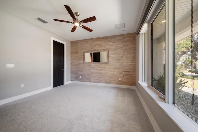 carpeted spare room featuring visible vents, baseboards, an accent wall, and a ceiling fan