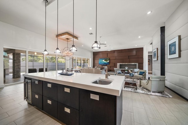 kitchen with decorative light fixtures, an island with sink, light countertops, dark cabinetry, and a sink