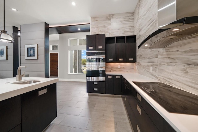 kitchen featuring black electric stovetop, light countertops, dark cabinetry, wall chimney exhaust hood, and a sink