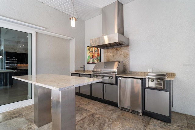 kitchen featuring decorative light fixtures, wall chimney exhaust hood, a textured wall, and freestanding refrigerator