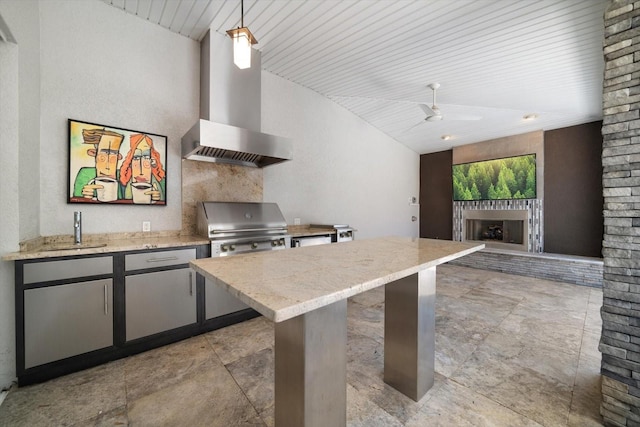 kitchen with a ceiling fan, light stone countertops, a fireplace, vaulted ceiling, and wall chimney exhaust hood