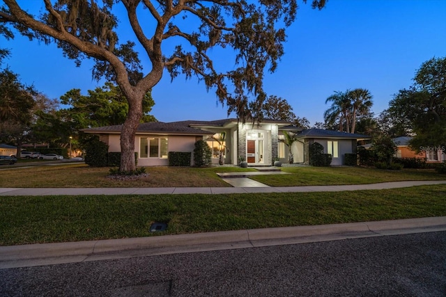 ranch-style house featuring stucco siding, stone siding, and a front lawn