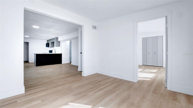 empty room with light wood finished floors, baseboards, visible vents, and a sink