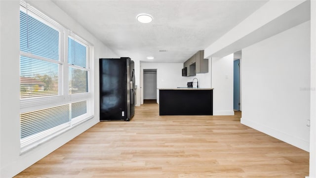 kitchen with a sink, baseboards, light countertops, light wood-type flooring, and freestanding refrigerator