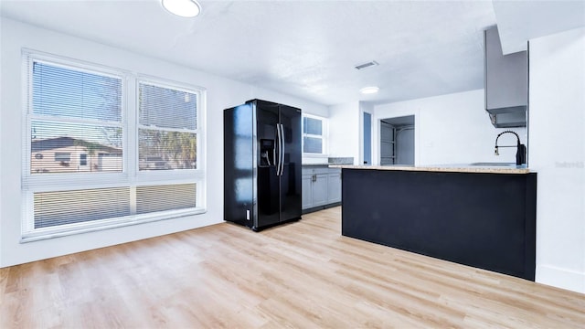 kitchen featuring a sink, light wood-style flooring, black fridge with ice dispenser, and visible vents