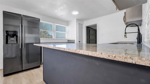 kitchen with stainless steel fridge with ice dispenser, a peninsula, light stone countertops, range hood, and light wood-style floors