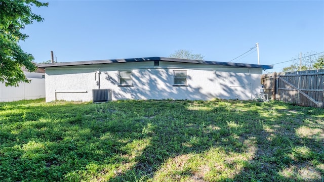 rear view of house featuring a yard, central AC unit, and a fenced backyard