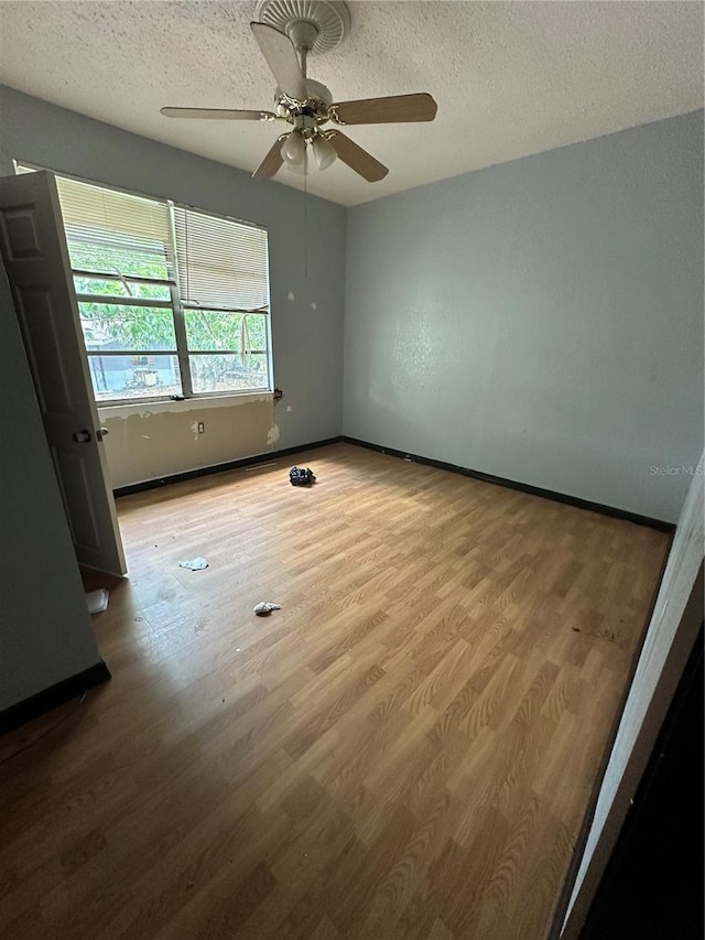 unfurnished bedroom featuring a ceiling fan, a textured ceiling, baseboards, and wood finished floors