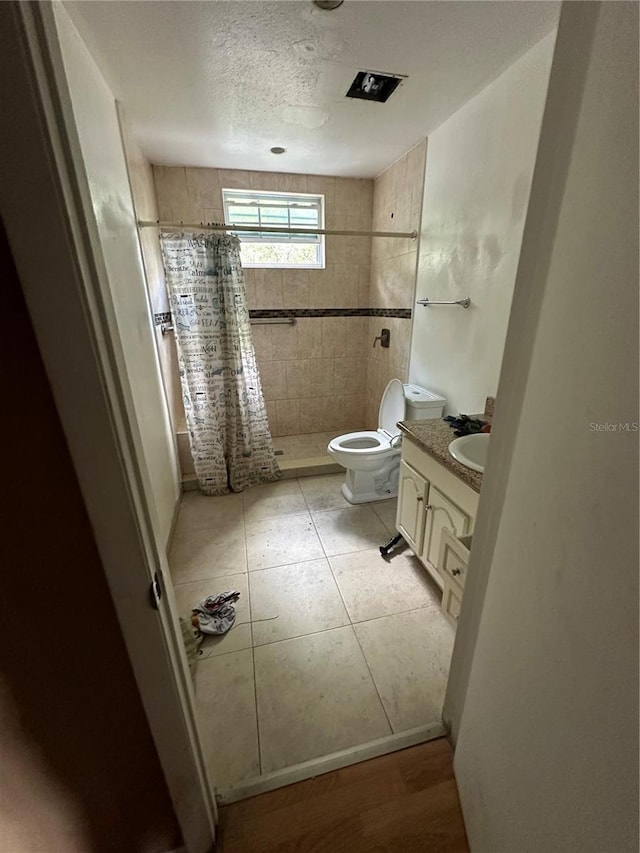 bathroom with toilet, a tile shower, vanity, a textured ceiling, and tile patterned flooring